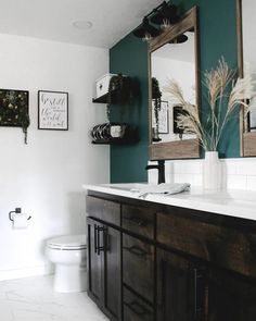 a white toilet sitting next to a bathroom sink under a mirror on top of a wooden cabinet