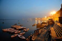 several boats are docked in the water at night near some buildings and people walking on the sidewalk