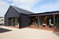 a black house with wooden decking and sliding glass doors on the front door is surrounded by gravel