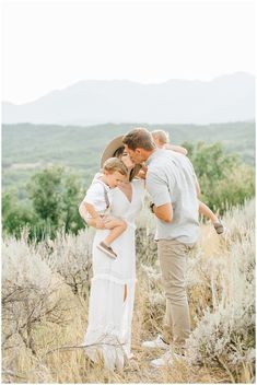 a man and woman holding a child in the middle of a field with mountains in the background