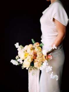 a woman in a white dress holding a bouquet of yellow and white flowers on her wedding day