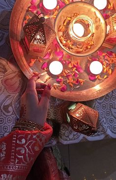 a person holding a lit candle in front of a plate with flowers and candles on it