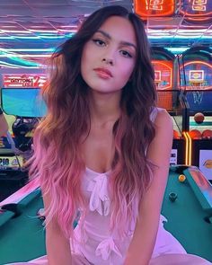 a young woman sitting on top of a pool table next to a neon light sign