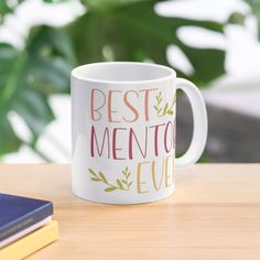 a white coffee mug with the words best mentor ever on it sitting next to some books