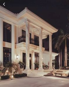 a car parked in front of a large white house at night with palm trees around it