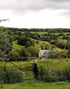 a man standing on top of a lush green hillside next to a fenced in field