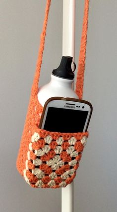 an orange and white crocheted cell phone bag hanging from a hook on a pole