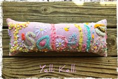 a pink pillow with colorful thread work on the front and back, sitting on a wooden surface