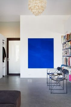 a living room filled with furniture next to a book shelf and a blue painting on the wall