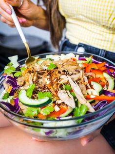 a woman is eating a salad with chicken and veggies