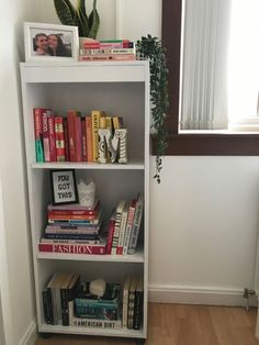 a bookshelf filled with lots of books in front of a window next to a potted plant