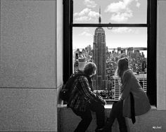 two people standing in front of a window looking at the city