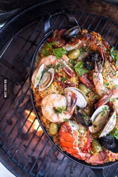 a pan filled with seafood and rice on top of a grill