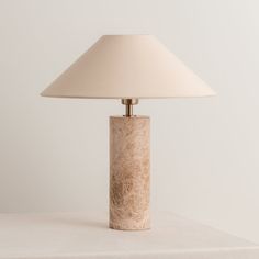 a lamp that is sitting on top of a white table with a beige shade over it