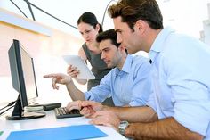 three people looking at a computer screen and pointing to something on the monitor while another person points