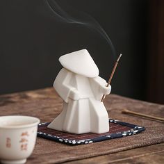 a white incense burner sitting on top of a wooden table next to a cup