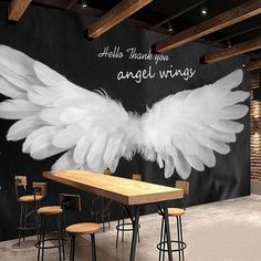 an angel wing painted on the wall above a table with stools and bar stools