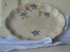 a white plate sitting on top of a bed next to a window sill with blue birds painted on it