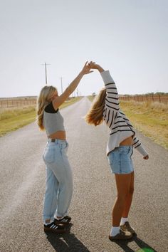 two young women standing on the side of a road touching their hands with each other