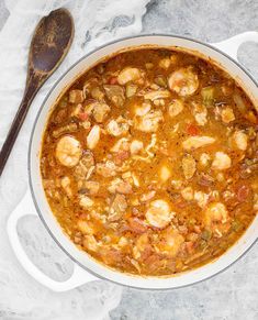 chicken seafood sausage gumbo in a white pot with a wooden spoon on the side