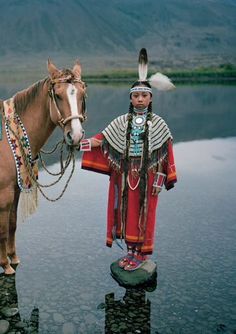 a man standing next to a horse on top of a body of water with mountains in the background