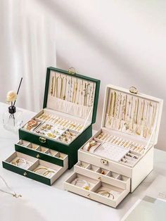 two green boxes filled with jewelry sitting on top of a white table next to a vase