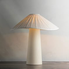 a white table lamp sitting on top of a wooden floor next to a gray wall