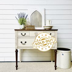 a white dresser with two drawers next to a potted plant and a sign on the wall