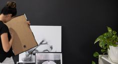 a woman holding a cardboard box in front of a black wall with pictures on it