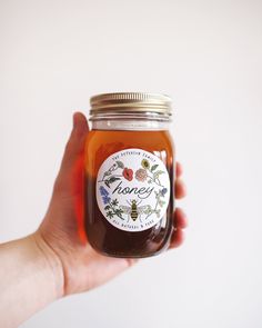 a hand holding a jar of honey with a label on the front and bottom half