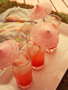 three glasses filled with pink liquid sitting on top of a white tray next to an umbrella