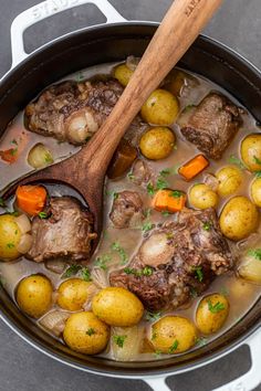 a pot filled with meat and potatoes on top of a table next to a wooden spoon