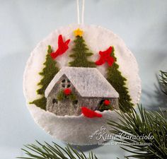 a christmas ornament with a house and birds on it hanging from a tree