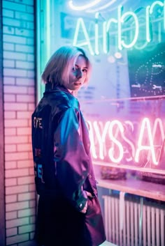 a woman standing in front of a window with neon lights behind her and the words always say on it