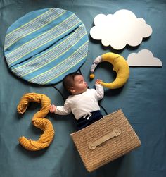 a baby laying on top of a blue blanket next to a bag and some clouds