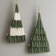 two green and white tasselled christmas trees hanging from hooks on a gray wall