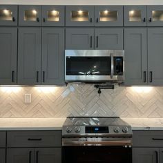 a kitchen with gray cabinets and stainless steel stove top oven in the center, along with white marble counter tops