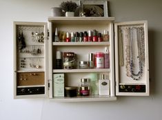 an open drawer with jewelry and necklaces in it on the wall next to a white wall