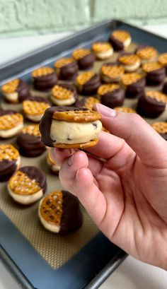 a person is holding a cookie in front of some cookies on a baking sheet with chocolates and pretzels