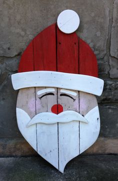 a wooden santa claus face with a red hat and beard on the side of a building