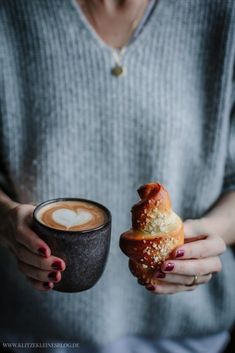 a woman holding a cup of coffee and a hot dog with toppings on it