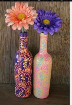 two vases with flowers in them sitting on a table next to a wooden wall