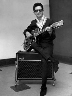 a man sitting on top of a guitar case holding an electric guitar in his right hand