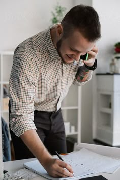 a man writing on a piece of paper while holding a cell phone to his ear