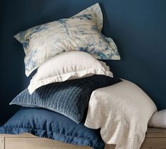 a pile of pillows sitting on top of a wooden dresser next to a blue wall