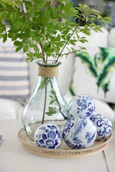 some blue and white eggs sitting on a tray next to a vase filled with green plants