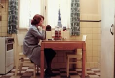 a woman sitting at a kitchen table drinking from a cup