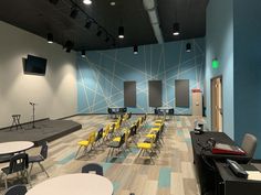 an empty room with tables and chairs in front of a projector screen on the wall