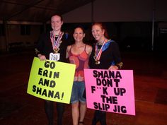 three people holding up signs and posing for the camera with medals around their necks in front of a tent