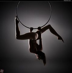 a woman is doing aerial acrobatics with a hoop on her back in the dark